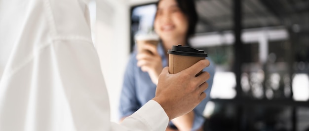 Photo couple of happy colleagues talking while standing at the office window with cups of coffee