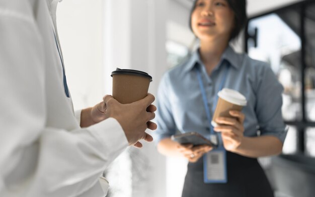 Photo couple of happy colleagues talking while standing at the office window with cups of coffee