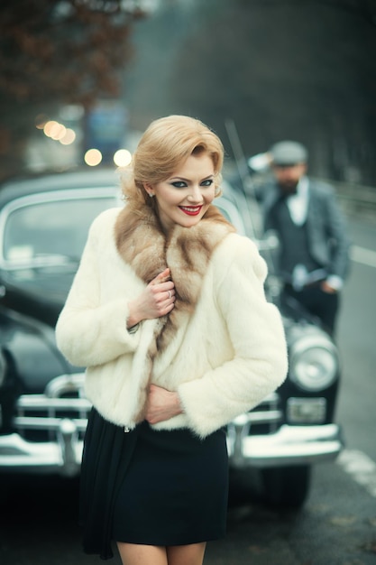 Couple happy at vintage retro car Friends on winter road trip in black car Beautiful young Caucasian man and sexy woman smiling joyful in fur coat