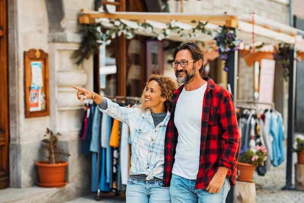 Couple of happy young adult people enjoy shopping and tourist outdoor leisure activity in the street Man and woman enjoy walking near stores smiling and pointing in friendship relationship love