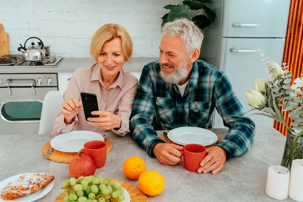 Пара завтракает дома и что-то читает со смартфона