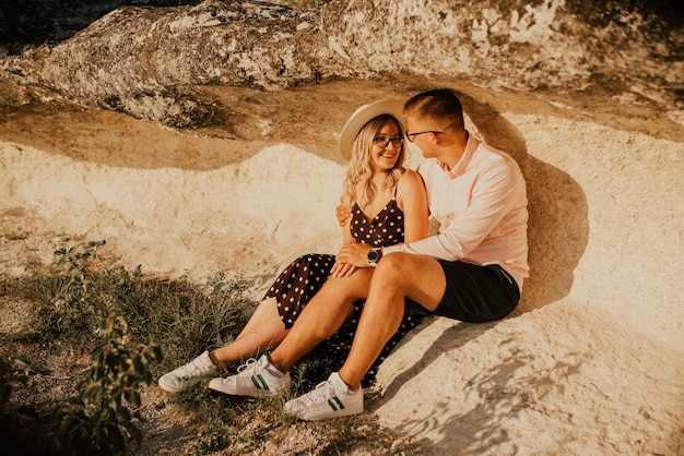 Couple in a hat are sitting on a large stone rock.