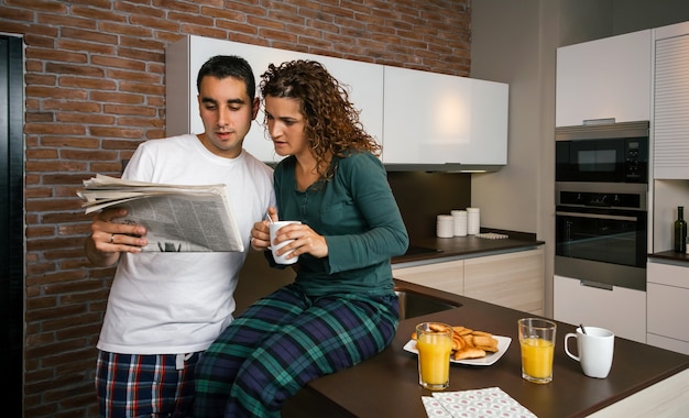 Couple having breakfast in the kitchen and reading the newspaper