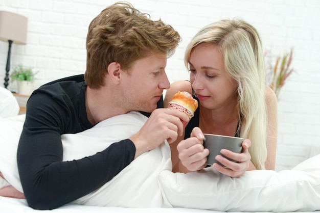 Photo couple having cupcake on bed at home