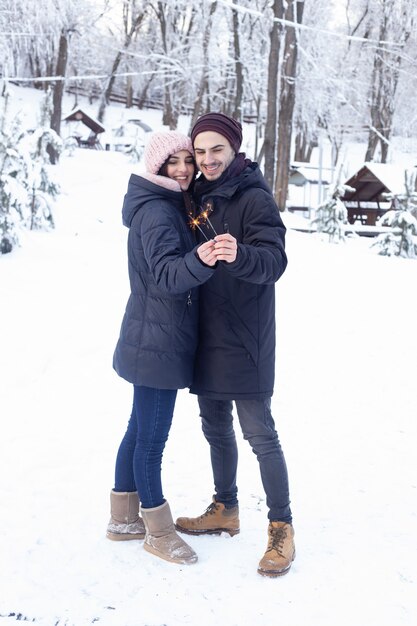 Couple having fun holding sparkles in winter park with snow