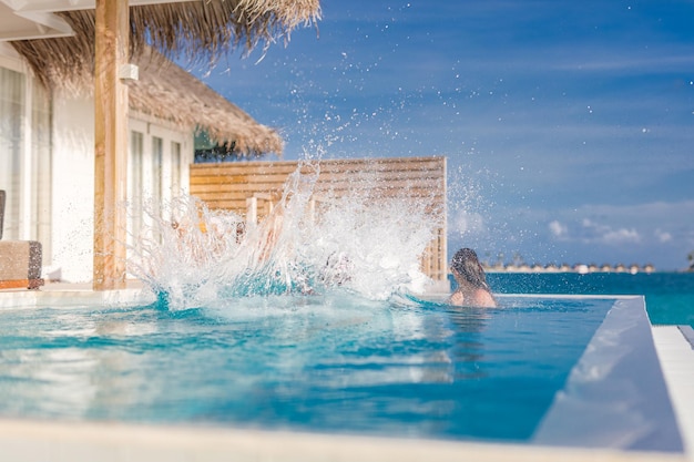 Couple having fun at the swimming pool Man jumping into infinity pool in luxury resort water splash