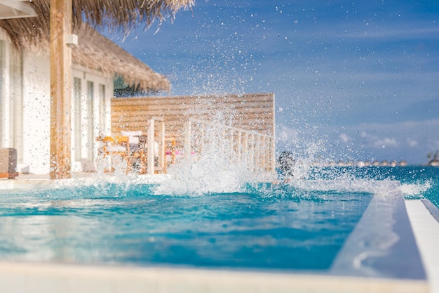 Coppia che si diverte in piscina uomo che salta nella piscina a sfioro in un resort di lusso con spruzzi d'acqua