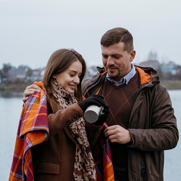 Photo couple having a hot drink by the lake with blanket