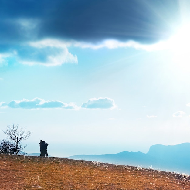 Couple on the hill against sunset. Landscape with clouds and sky.