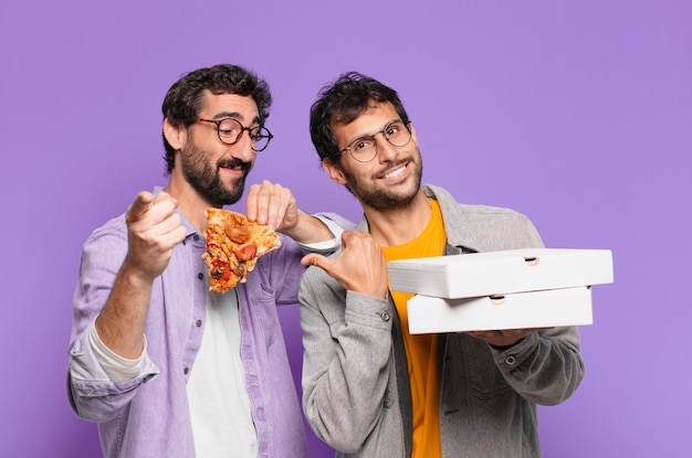 Couple of hispanic friends pointing or showing and holding take away pizzas