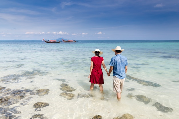 Couple holding hand walking in to crystal clear sea with long tail boat