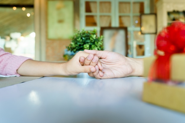 A couple holding hands each other in restaurant with a golden gift box with red ribbon.