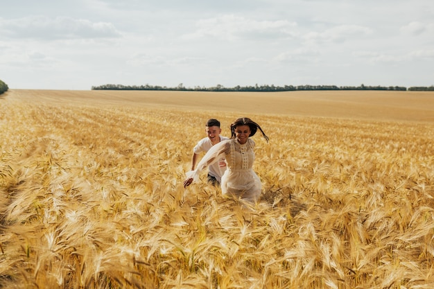 Couple holding hands and running in wheat field.