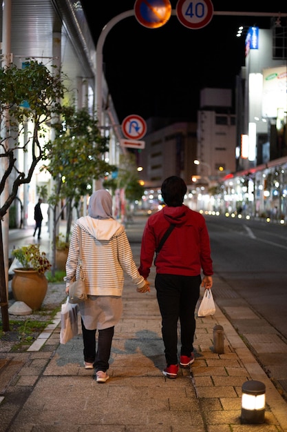 A couple holding hands walking down a street holding hands.