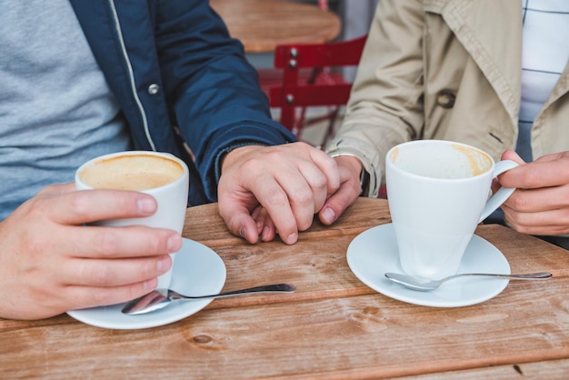 Фото Пара держится за руки во время питья лате на открытом воздухе кафе близко