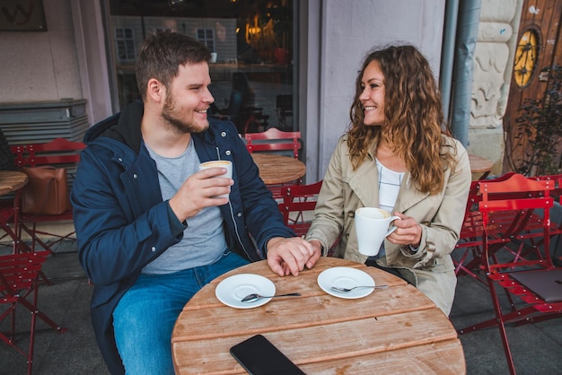 Photo couple holding hands while drinking latte in outdoors cafe