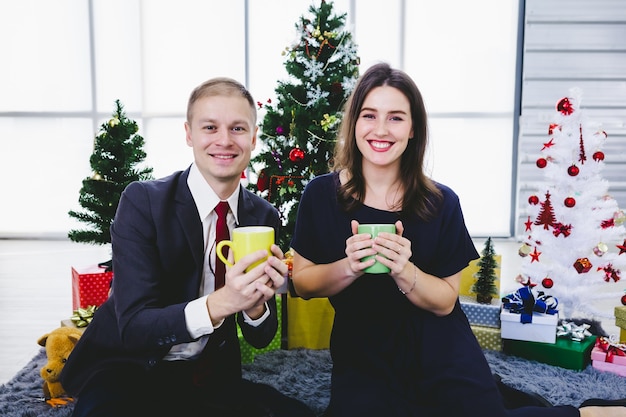 Couple holding mugs near Christmas tree