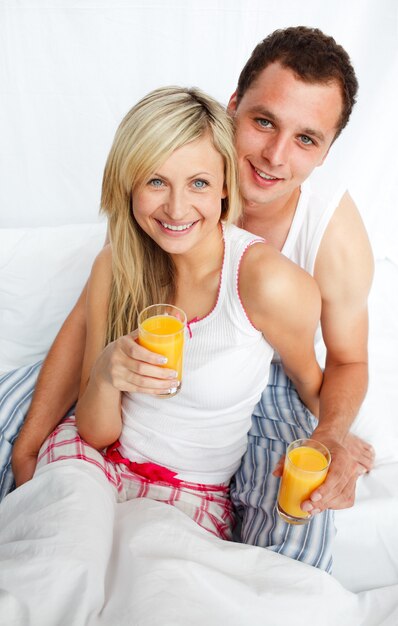 Couple holding orange juice glasses in bed