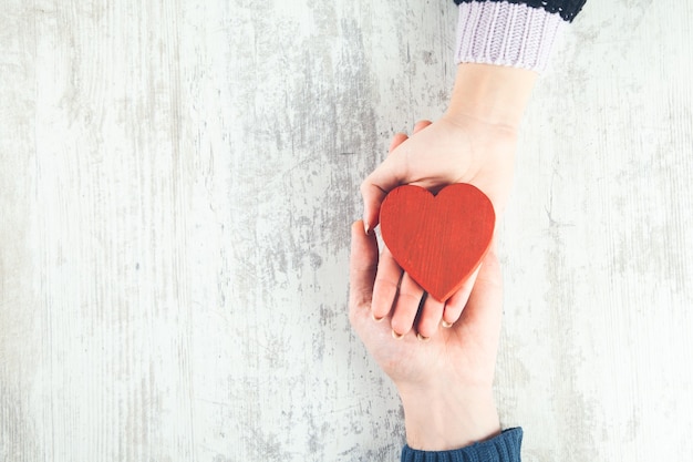 Couple holding red heart on wooden surface