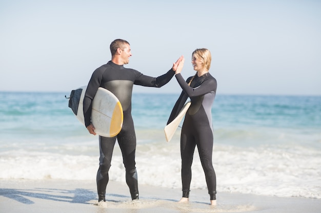 Couple holding a surfboard and giving a high five to each other