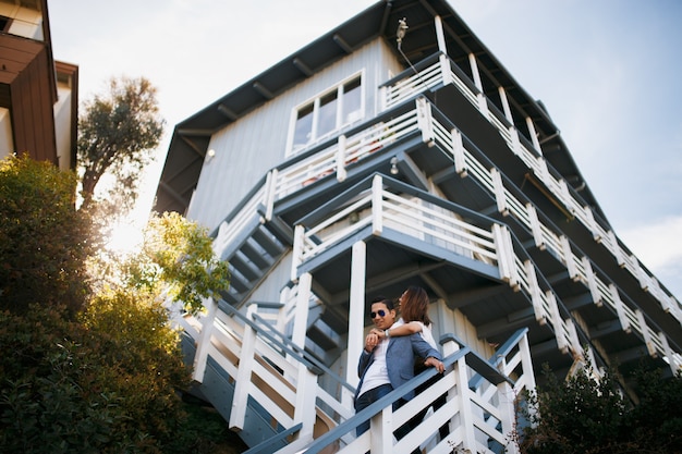 Photo couple hugging on the staircase of big house, indian brunette guy hug asian girl. date young people in sunny weather.