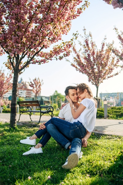 Couple hugs near sakura trees in blooming garden.