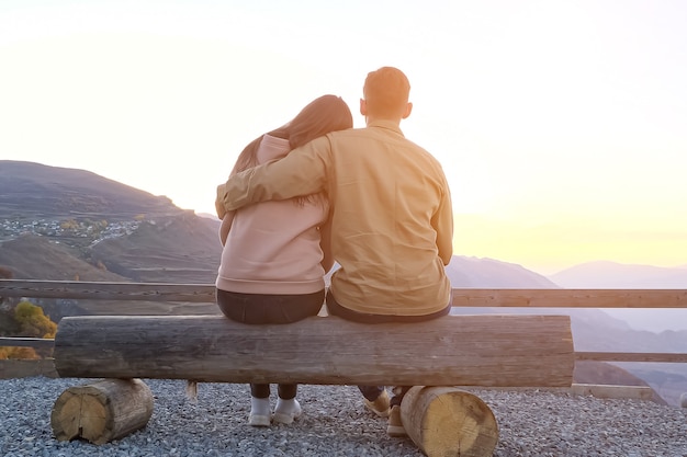 Foto coppia abbracci seduti su una panchina sul punto di osservazione contro le pittoresche montagne antiche al tramonto vista posteriore