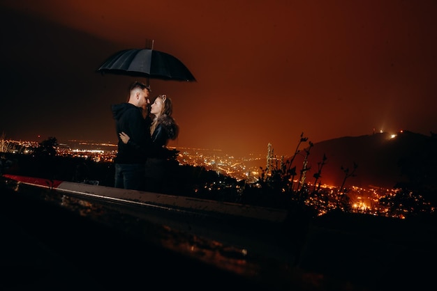 雨の中、傘の下でカップルがキスをしている。