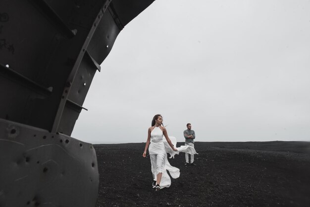 couple is standing near the plane which fell a long time ago black beach