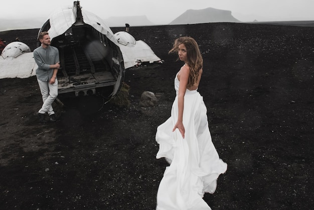 couple is standing near the plane which fell a long time ago black beach