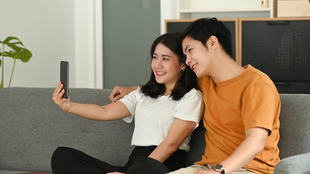 A couple is using smartphone to make selfie and sitting on sofa in living room