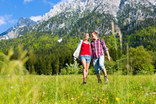 カップルは山と牧草地を歩いています。