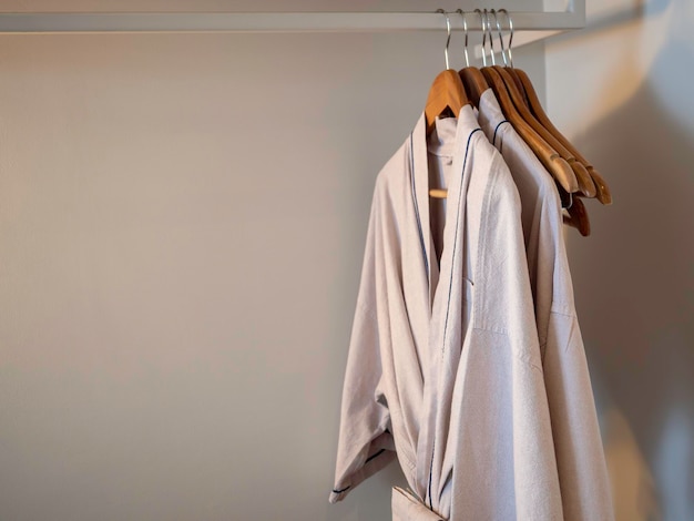 couple of japanese style cotton bathrobes hanging on the wooden hangers on the rack inside the white wardrobe for the hotel guest in the dim lights with copy space
