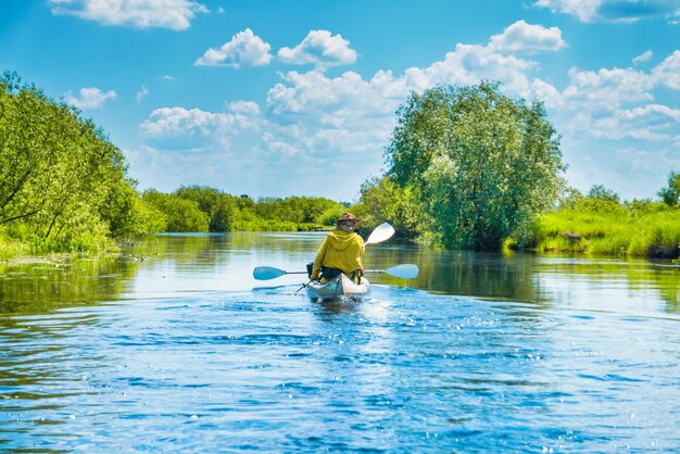 Couple at kayak trip on blue river landscape and green forest with trees blue water clouds sky