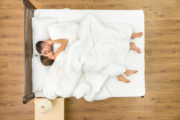 The couple kiss on the bed. View from above