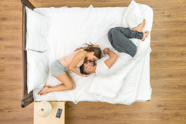 The couple kiss in the bed. View from above