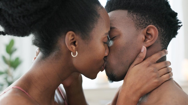 カップルは寝室でセックスと家のベッドで愛をキスします。結婚のエロティックな性的エネルギーと家で一緒に性的である裸の人々幸せなアフリカ人男性と女性がアパートで情熱を持ってキスします。