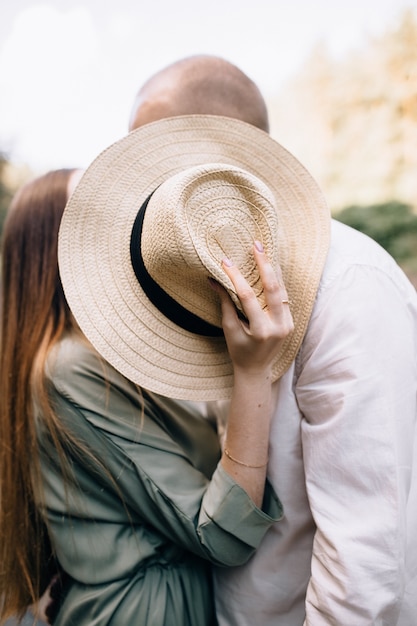 Couple kissing covering their faces with a straw hat.