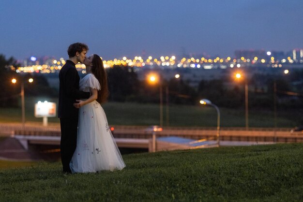 Photo a couple kissing in a field with the city lights in the background