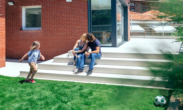 Couple kissing in front of their new house while their son plays soccer