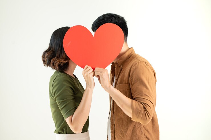 Photo 白い壁で隔離のハートのシンボルの後ろにキスカップル