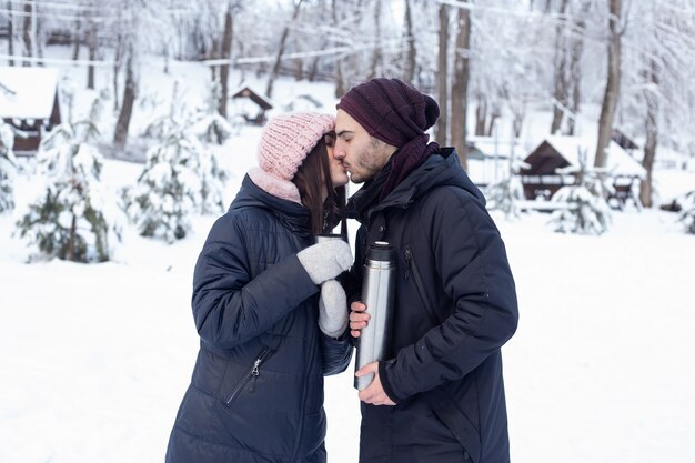 Couple kissing while pouring tea from a thermos in winter park