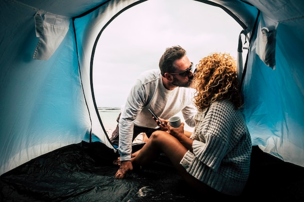 Photo couple kissing while sitting at tent outdoors