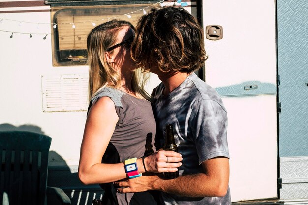 Foto coppia che si bacia in piedi contro un rimorchio da viaggio
