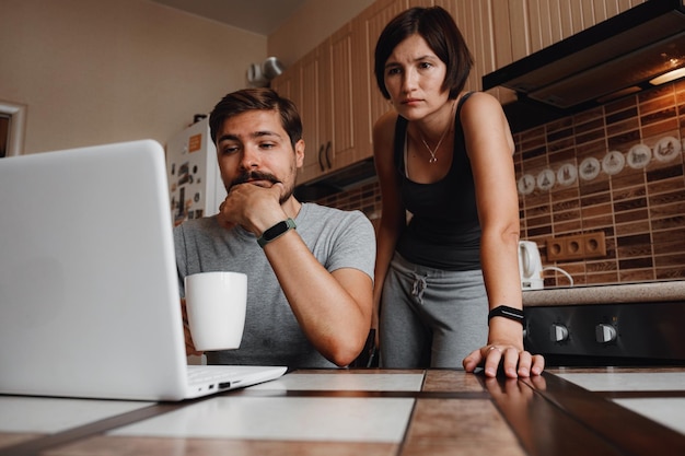 Coppia in cucina leggendo notizie e utilizzando il computer portatile