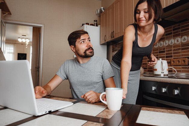 Couple at kitchen reading news and using laptop