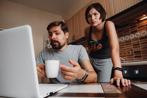 Coppia in cucina leggendo notizie e utilizzando il computer portatile