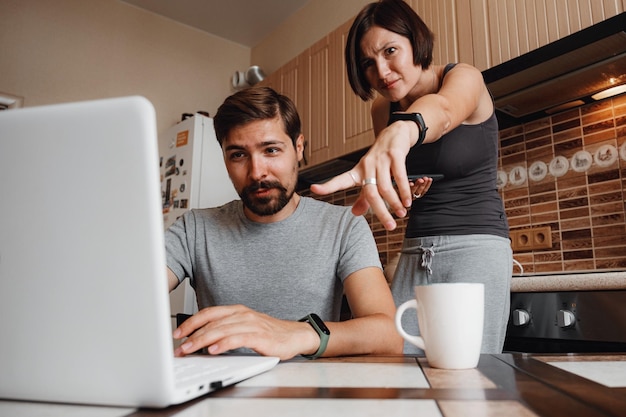 Photo couple at kitchen reading news and using laptop