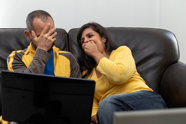 Couple of Latin American friends working together at home sitting on the sofa