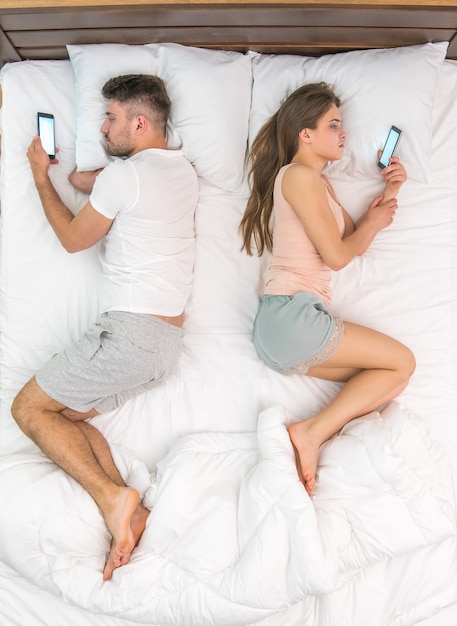 The couple lay on the bed and phone. View from above